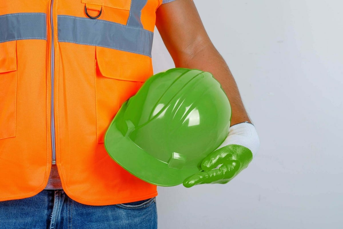 Male builder in uniform, jeans, gloves holding helmet in his hand , front view.